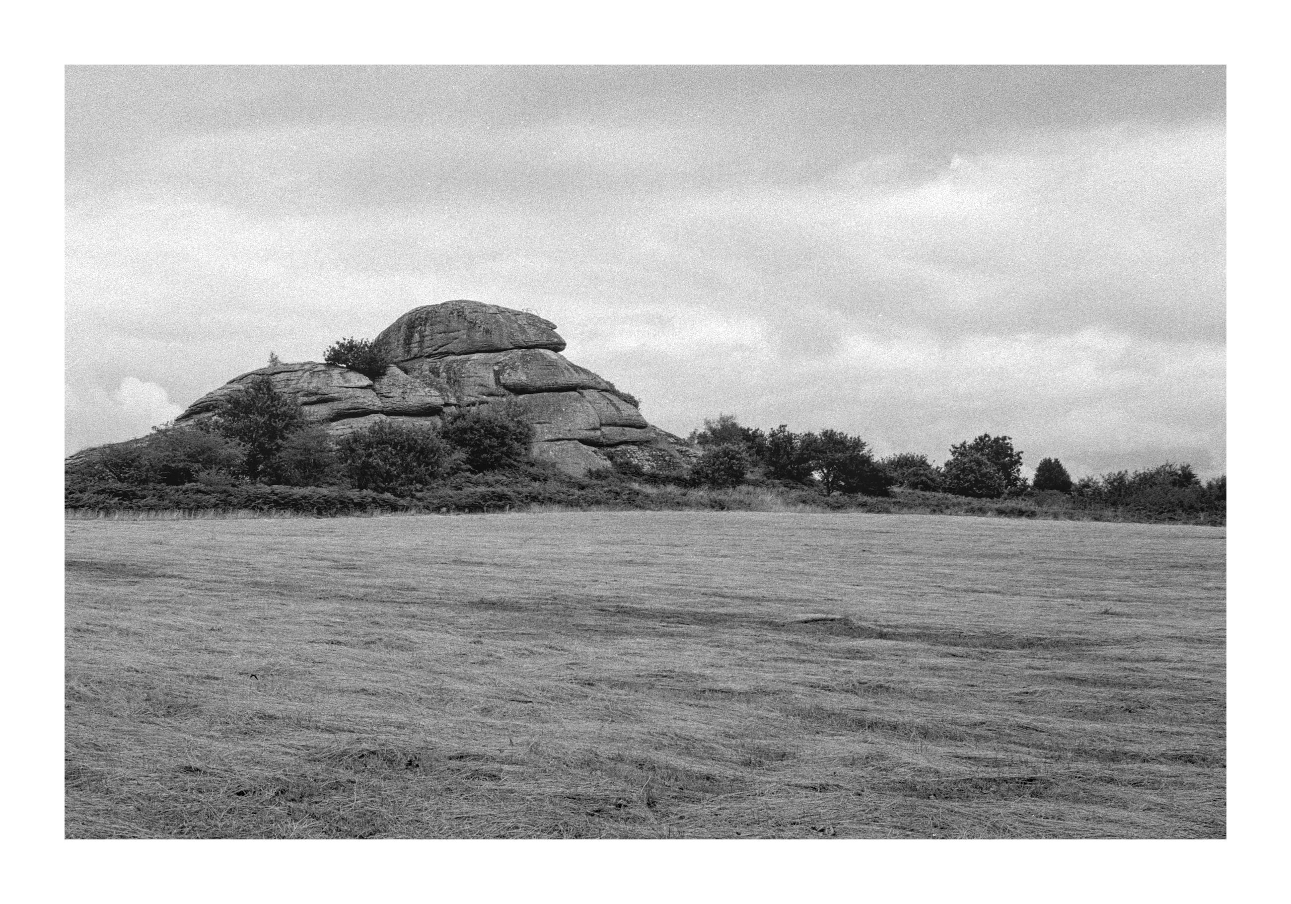 Photograph of a large tor, seen from across a field after harvest.